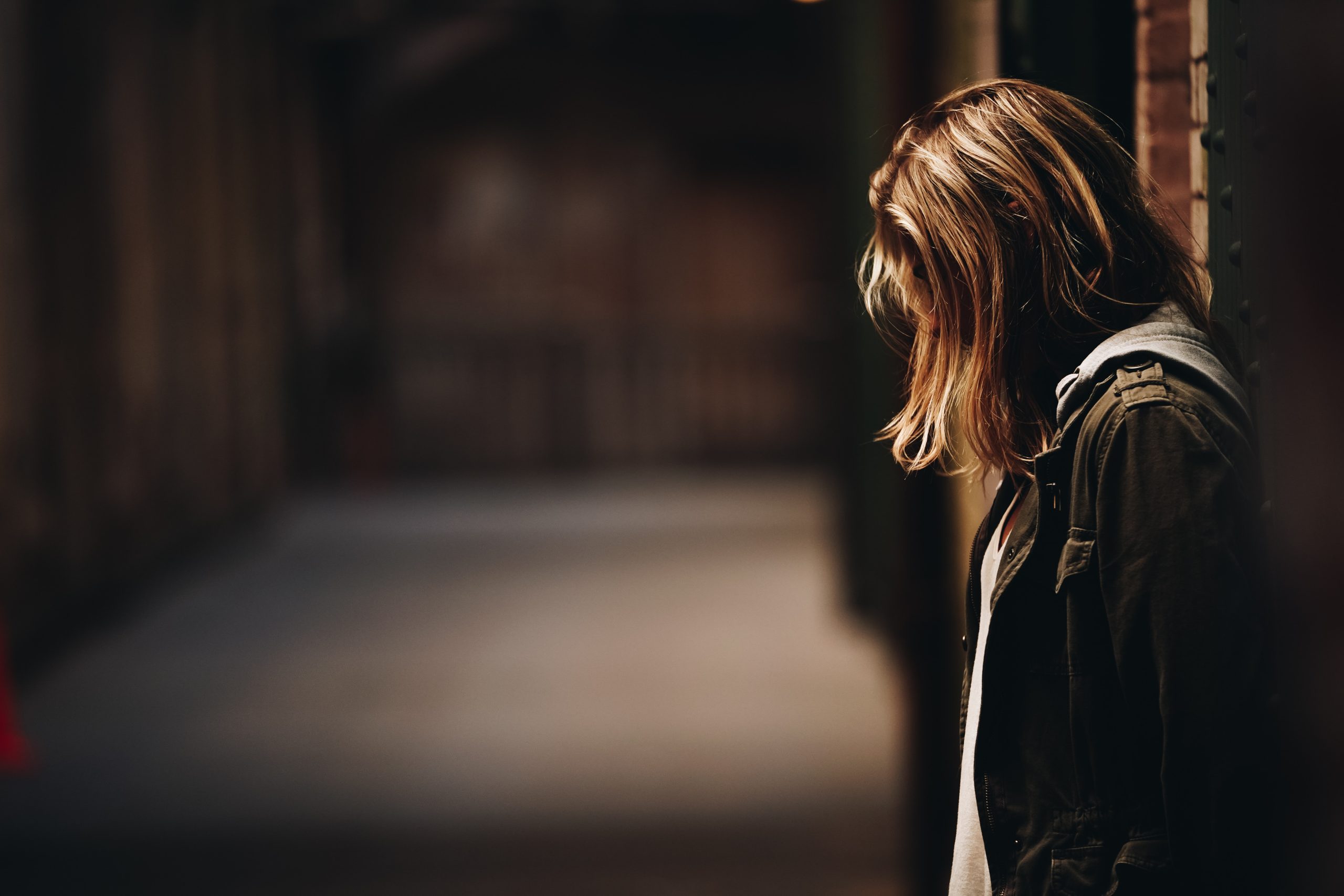 A young woman leaning against a brick wall in a dark environment