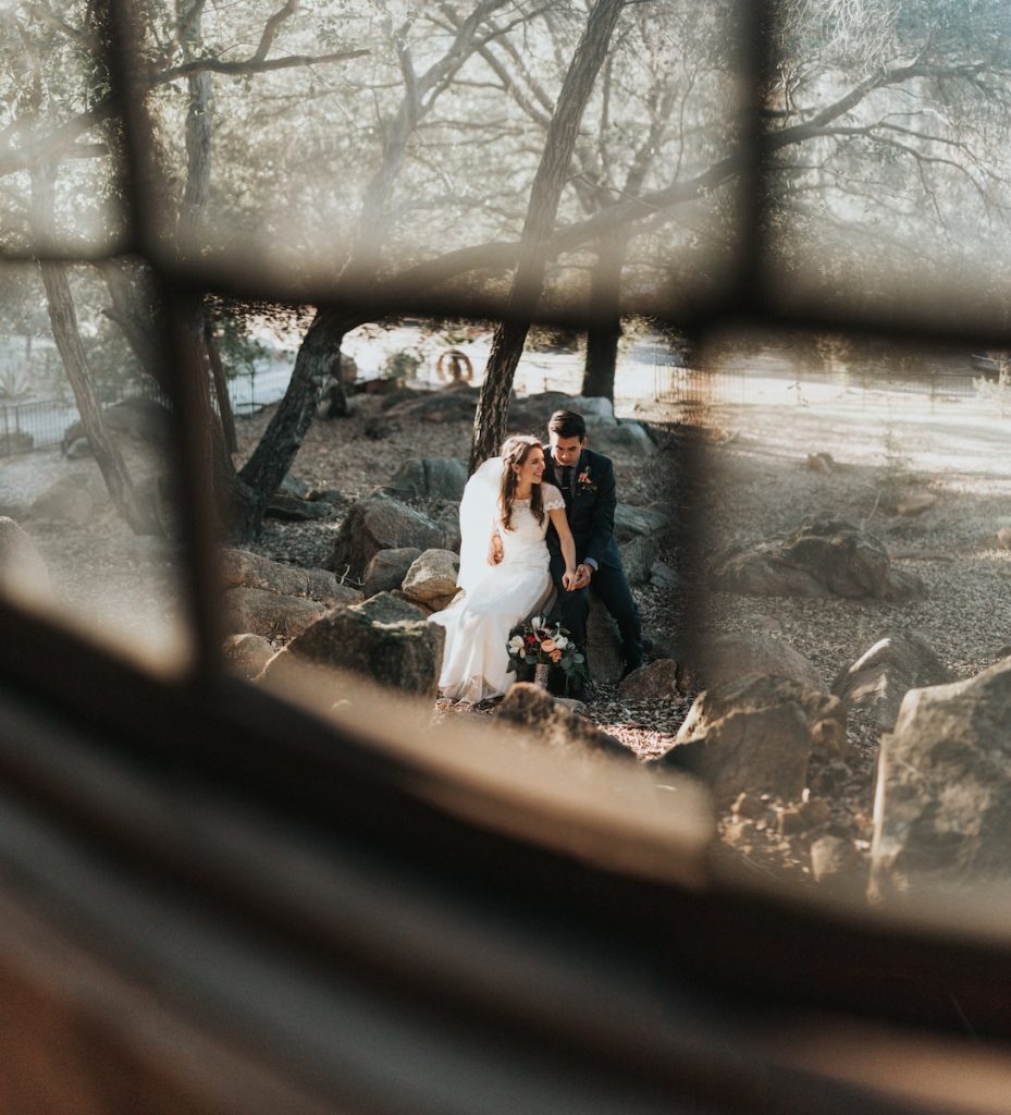 bride and groom sitting on rock holding hands