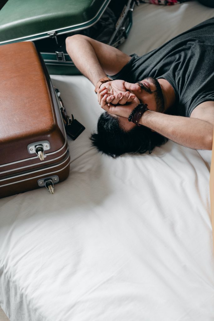 Man laying down on a bed resting with suitcases around him